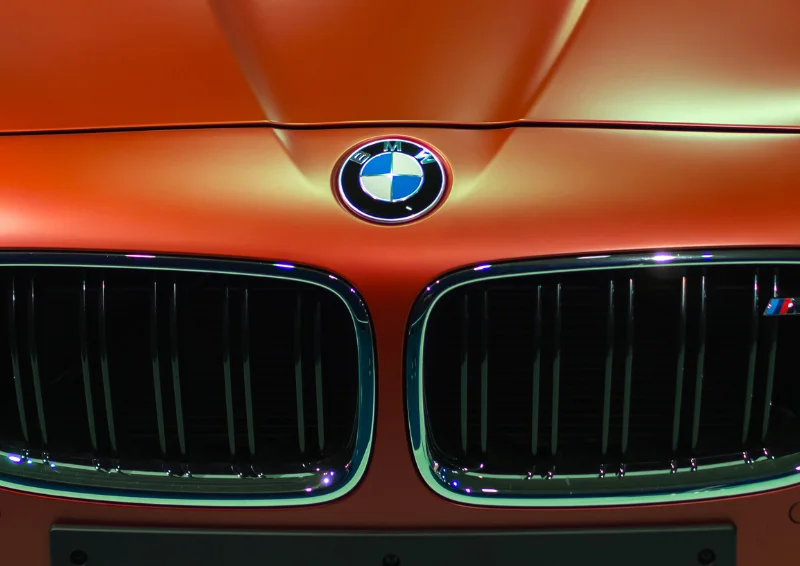 BMW badge and twin kidney grilles on orange car hood under showroom light