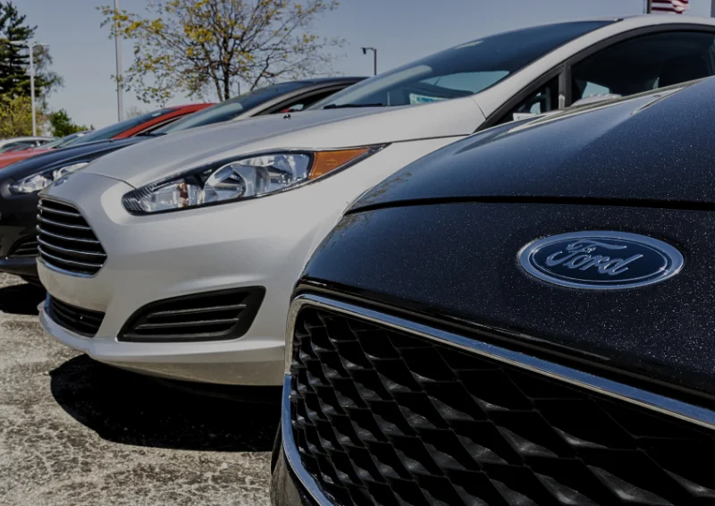 Ford vehicles lined up outside dealership, showing grilles and badges.