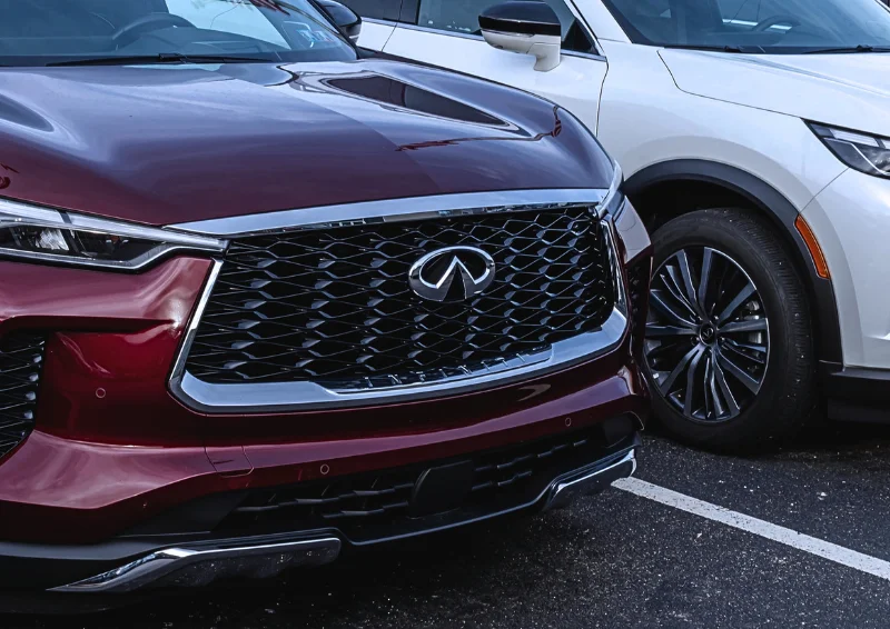 Infiniti logo on black mesh grille of a red SUV parked next to white car