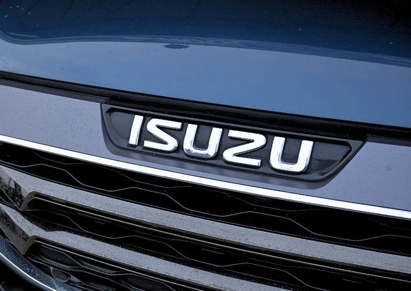Close-up of chrome Isuzu badge on black grille with dark blue hood