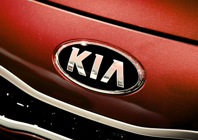 Kia logo on glossy red hood with chrome detailing around the emblem