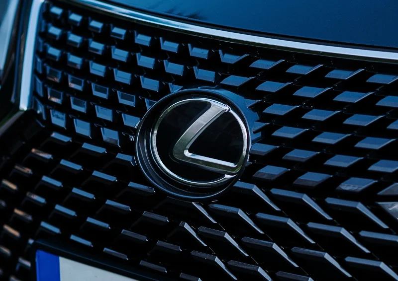 Lexus badge on black diamond-pattern grille of a dark luxury vehicle.