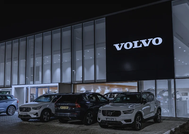 Volvo dealership at night with SUVs parked in front and showroom lit