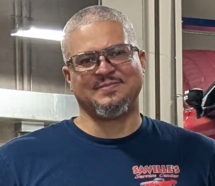 Mechanic in glasses and Saville’s shirt smiles inside an auto repair garage in Purcellville, VA